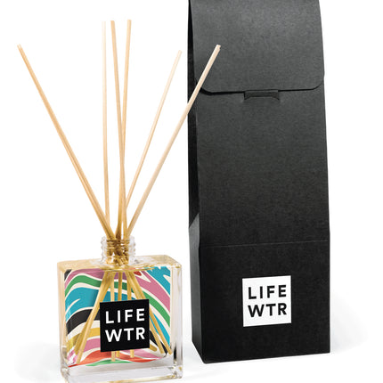 Close-up view of 8 oz clear reed diffuser with branded label design and natural reed sticks inserted in bottle opening