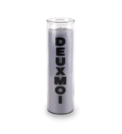 A 16 oz Prayer Candle from Custom Candles LA filled with gray wax in a tall glass container. The candle is printed with a logo that reads "DEUXMOI" in bold black letters that are stacked vertically down the front of the glass.