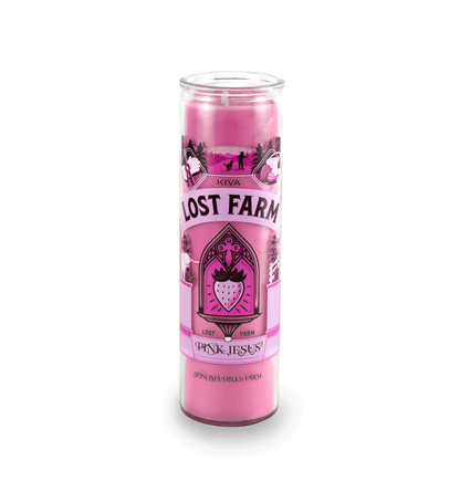 A 16 oz Prayer Candle from Custom Candles LA filled with pink wax in a tall glass container. The candle is printed with a logo that reads "KIVA LOST FARM PINK JESUS" in black. Printed in various pinks and black is imagery of a strawberry in a church like window surrounded by the logo and a silhouette of a farm. The pink wax shows through the imagery. 