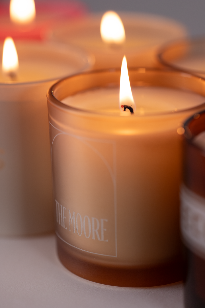 Nude frosted 9 oz candle with a custom logo engraved into the glass, lit