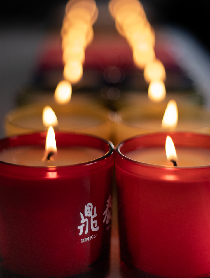 Red glass 9 oz candles with a custom white printed logo, lit, soft glowing background