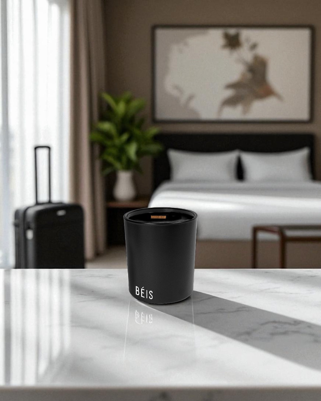 A black candle with a white logo placed subtly near the bottom of the glass, sitting on a white marble countertop within a hotel room