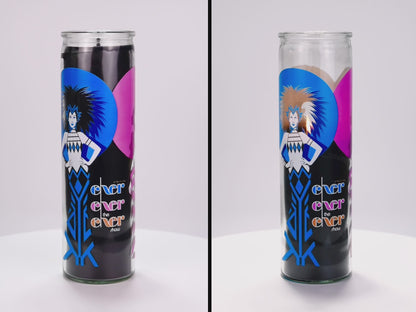 Two 16 oz Prayer Candles from Custom Candles LA filled with black wax in a tall glass container spinning side by side. The left candle is unlit, and the right candle is lit and burned halfway down. The candles are printed with an image on a woman with spiky hair and her hands on her hips in royal blue and white in front of a blue and a pink circle with the black wax showing through. Next to the woman the glass Is printed with the words "Exer exer the exer show" stacked in blue, pink, and orange. 