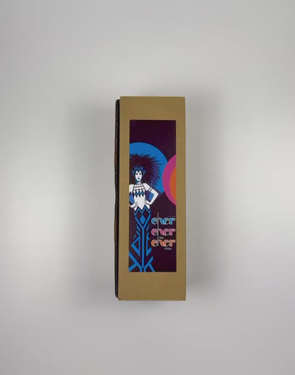 An unboxing video of the 16 oz Prayer Candle from Custom Candles LA filled with black wax that comes in a Kraft mailer box with a colorful sticker label of logo artwork. The candle is printed with an image on a woman with spiky hair and her hands on her hips in royal blue and white in front of a blue and a pink circle with the black wax showing through. Next to the woman the glass Is printed with the words "Exer exer the exer show" stacked in blue, pink, and orange.