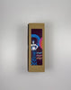 An unboxing video of the 16 oz Prayer Candle from Custom Candles LA filled with black wax that comes in a Kraft mailer box with a colorful sticker label of logo artwork. The candle is printed with an image on a woman with spiky hair and her hands on her hips in royal blue and white in front of a blue and a pink circle with the black wax showing through. Next to the woman the glass Is printed with the words "Exer exer the exer show" stacked in blue, pink, and orange.