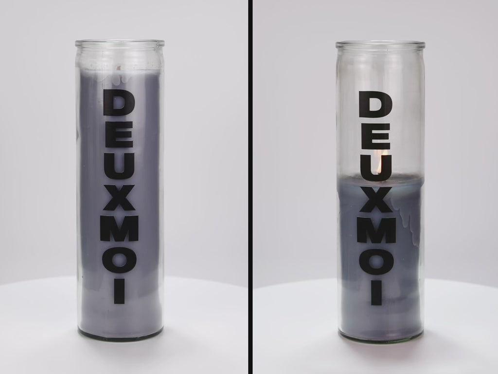 Two 16 oz Prayer Candles from Custom Candles LA filled with gray wax in a tall glass container spinning side by side. The candles are printed with a logo that reads "DEUXMOI" in bold black letters that are stacked vertically down the front of the glass.