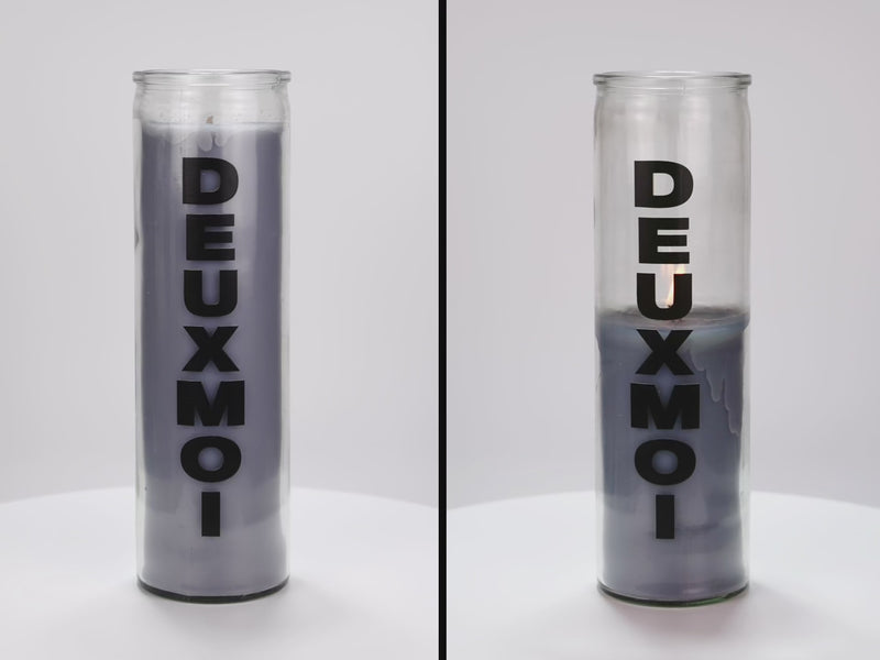 Two 16 oz Prayer Candles from Custom Candles LA filled with gray wax in a tall glass container spinning side by side. The candles are printed with a logo that reads "DEUXMOI" in bold black letters that are stacked vertically down the front of the glass.