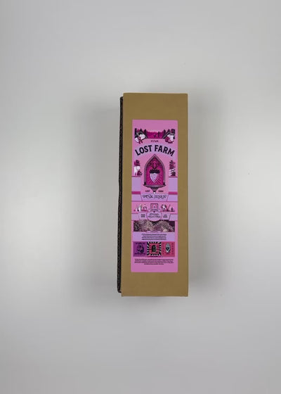 An unboxing video of the 16 oz Prayer Candle from Custom Candles LA filled with pink wax that comes in a Kraft mailer box with a pink sticker label of the logo artwork. The candle is printed with a logo that reads "KIVA LOST FARM PINK JESUS" in black. Printed in various pinks and black is imagery of a strawberry in a church like window surrounded by the logo and a silhouette of a farm. The pink wax shows through the imagery. 