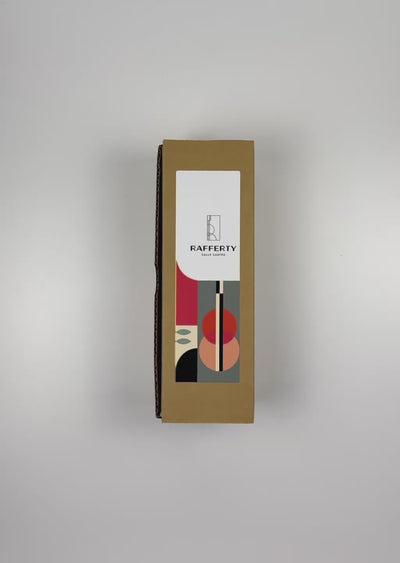 An unboxing video of the 16 oz Prayer Candle from Custom Candles LA filled with red wax that comes in a Kraft mailer box with a colorful sticker label of artwork. The candle is printed with a white "RAFFERTY CALLE CUATRO" Logo. surrounding the logo is a pattern of various shapes in black teal, bright pink, pale yellow and peach. The red wax shows through behind the logo.