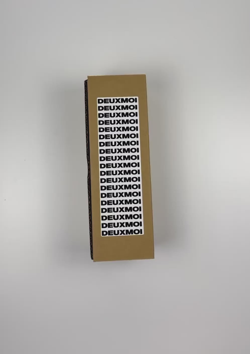 Load video: An unboxing video of the 16 oz Prayer Candle from Custom Candles LA filled with gray wax that comes in a Kraft mailer box with a black and white sticker label of the logo. The candle is printed with a logo that reads &quot;DEUXMOI&quot; in bold black letters that are stacked vertically down the front of the glass.