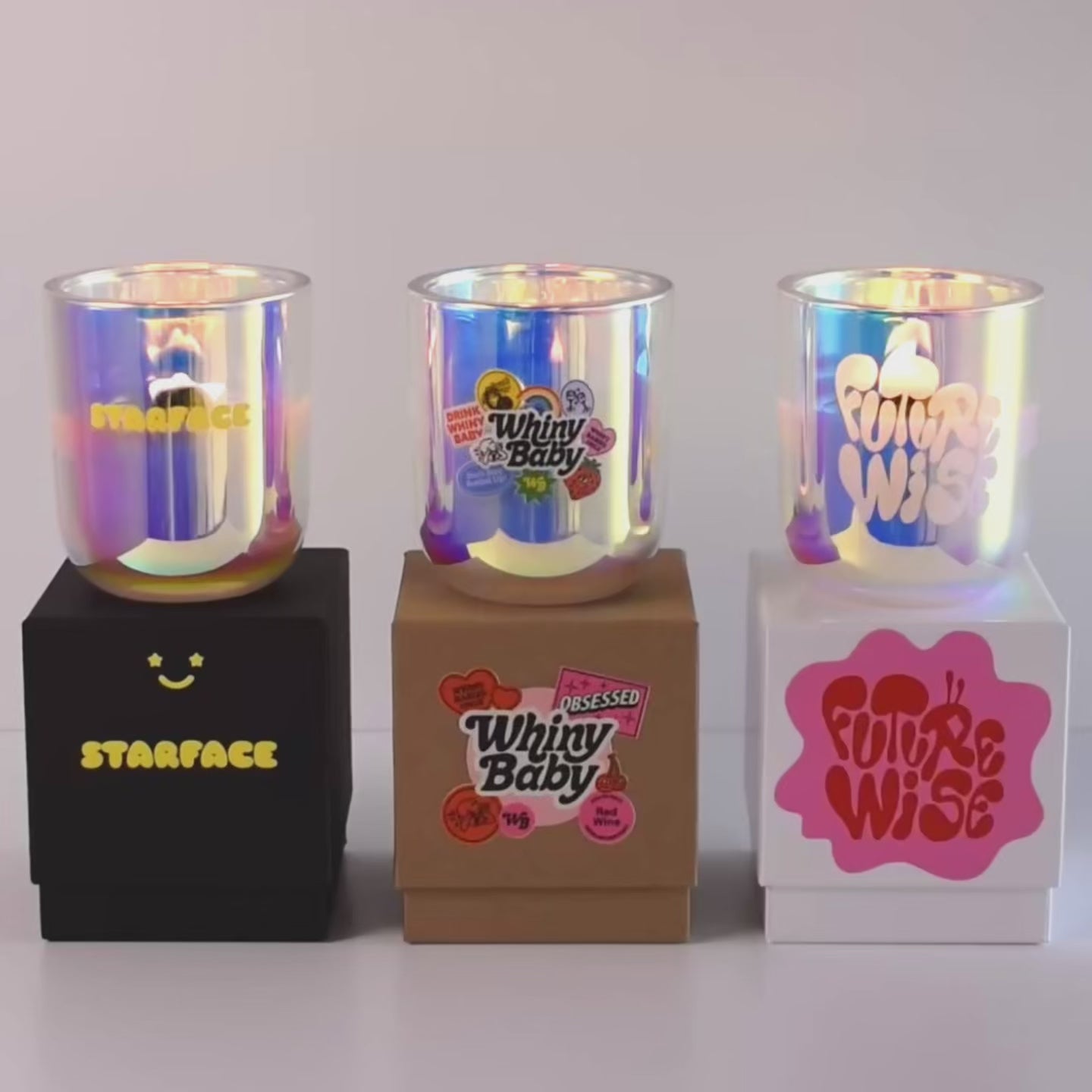 Load video: Three lit 12 oz Luxe Custom Candles in the color “Bliss” which is an iridescent pink from Custom Candles LA. The 1st candle has the &quot;Starface&quot; logo printed on the glass in yellow and sits on a black box that has the logo printed in yellow. The 2nd candle has a multicolor &quot;Whiny Baby&quot; logo printed on the glass and sits on top of a Kraft box with the multicolor logo printed on it. The 3rd candle has the &quot;Futurewise&quot; logo etched on the glass, and sits on a white box with the logo printed on it in pink and red.