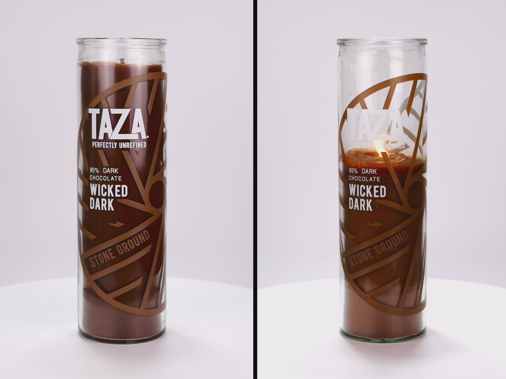 Two 16 oz Prayer Candles from Custom Candles LA filled with brown wax in a tall glass container spinning side by side. The left candle is unlit, and the right candle is lit and burned halfway down. The candles are printed with a logo that reads "TAZA Perfectly Unrefined" in white and "95% Dark Chocolate Wicked Dark" printed underneath it, with a brown circle that includes lines printed in brown along with "Stone Ground" behind the logo. The brown wax shows through the image.