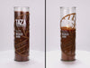 Two 16 oz Prayer Candles from Custom Candles LA filled with brown wax in a tall glass container spinning side by side. The left candle is unlit, and the right candle is lit and burned halfway down. The candles are printed with a logo that reads "TAZA Perfectly Unrefined" in white and "95% Dark Chocolate Wicked Dark" printed underneath it, with a brown circle that includes lines printed in brown along with "Stone Ground" behind the logo. The brown wax shows through the image.