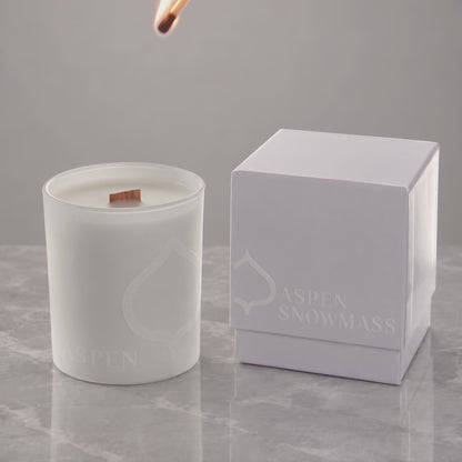 White 14 oz. printed luxury candle lit, with a tone-on-tone Aspen Snowmass logo glowing beside its white gift box