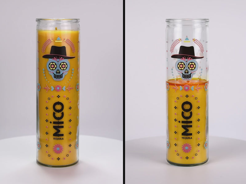 Two 16 oz Prayer Candles from Custom Candles LA filled with yellow wax in a tall glass container spinning side by side. The candles are printed with a colorful image of a calavera surrounded by ornate patterns in various colors and shapes including flowers, dots, and diamonds. In the middle of the candle there is a vertical logo printed in black that reads "MICO TEQUILA". The yellow wax shows through the artwork.