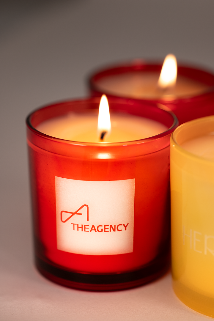 Red glass 9 oz candle with a real estate brokerage logo engraved into the glass, lit